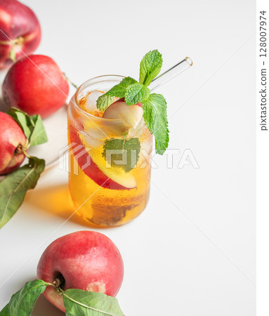 Ice tea with peach, mint in a glass on a white table near window with fresh fruits and sunlight. Ice tea with peach, mint in a glass on a white table near window with fresh fruits and sunlight. 128007974