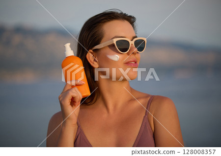 Beautiful Woman in Bikini Applying Sun Cream on Tanned Face. Sun Protection. Skin and Body Care concept. Girl Using Sunscreen to Skin. Portrait Of Female Holding Suntan Lotion or Moisturizing Sunblock Beautiful Woman in Bikini Applying Sun Cream on Tanned Face. Sun Protection. Skin and Body Care concept. Girl Using Sunscreen to Skin. Portrait Of Female Holding Suntan Lotion or Moisturizing Sunblock 128008357