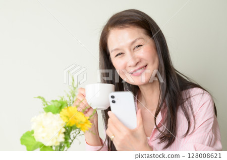 Senior woman looking at smartphone with coffee in hand Senior woman looking at smartphone with coffee in hand 128008621