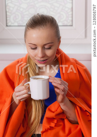 Woman lying on sofa under blanket drinking tea Woman lying on sofa under blanket drinking tea 128008797