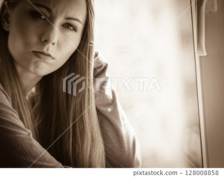 Sad depressed teen girl sitting on window sill 128008858