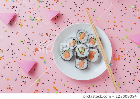 Vibrant sushi roll arrangement on pink confetti background with chopsticks 128009054