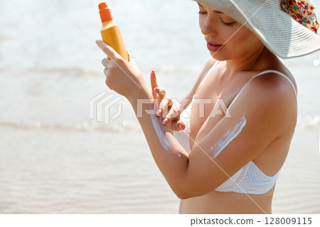 Woman Applying Sun Cream on Tanned Skin. Sun Protection. Skin Care. Girl Smears Sunscreen on Skin. Portrait of Female Holding Suntan Lotion or Moisturizing Sunblock 128009115