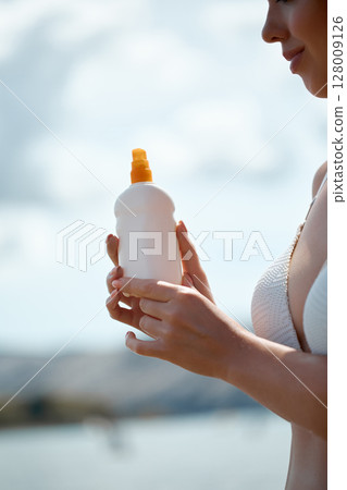 Close-Up of a Woman Holding Sunscreen on a Sunny Day at the Beach 128009126