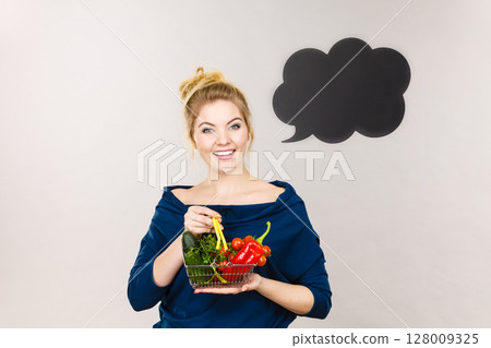 Woman holds shopping basket with vegetables, speech bubble Woman holds shopping basket with vegetables, speech bubble 128009325
