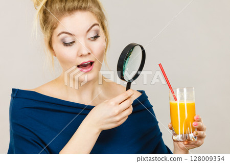 Woman holding magnifying glass investigating juice 128009354