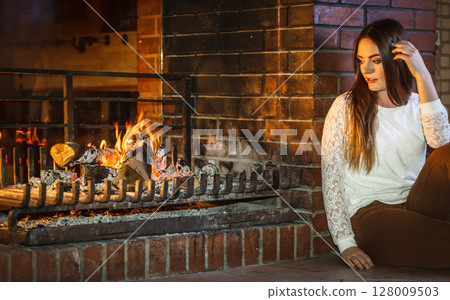 Pensive woman relaxing at fireplace. Winter home. 128009503