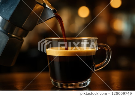 Rich espresso coffee with crema pouring from moka pot into clear glass cup Rich espresso coffee with crema pouring from moka pot into clear glass cup 128009749