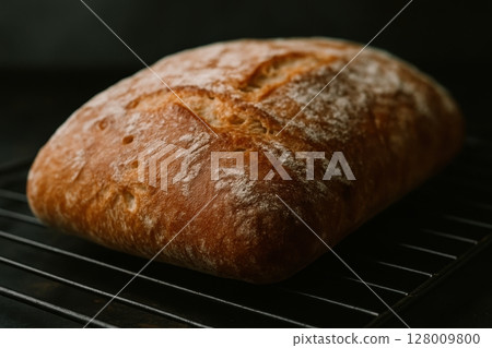 Golden brown rustic artisan bread loaf with crispy crust on a dark cooling rack Golden brown rustic artisan bread loaf with crispy crust on a dark cooling rack 128009800