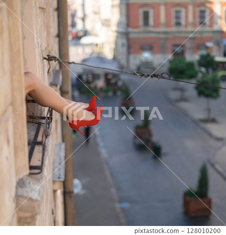 Close-up of female legs with red shoes of high heels. The woman is raising her feet through the window 128010200