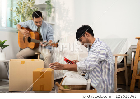 Gay couple enjoying music and unpacking in their new home 128010365