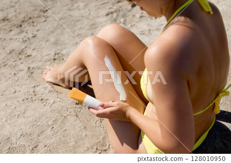 Closeup on female Hand applying sunscreen cream on Leg. Skincare. Sun protection sun cream, on her smooth tanned legs Closeup on female Hand applying sunscreen cream on Leg. Skincare. Sun protection sun cream, on her smooth tanned legs 128010950