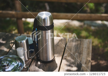 Thermos and Various Table Items on a Wooden Outdoor Picnic Table in Nature Thermos and Various Table Items on a Wooden Outdoor Picnic Table in Nature 128011723