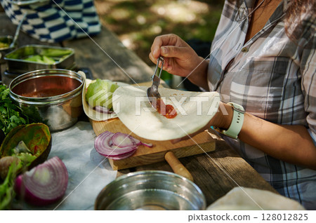 Person Preparing a Fresh Tortilla Meal Outdoors on a Rustic Wooden Table Person Preparing a Fresh Tortilla Meal Outdoors on a Rustic Wooden Table 128012825