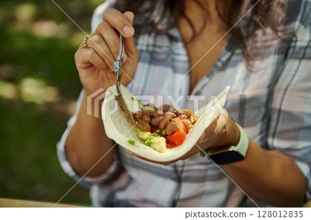 A Close-Up of a Woman Holding and Filling a Fresh Bean Vegan Wrap 128012835