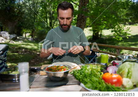 Man Preparing a Fresh Meal Outdoors at a Scenic Picnic Spot in Nature Man Preparing a Fresh Meal Outdoors at a Scenic Picnic Spot in Nature 128012853