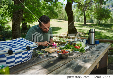 Man Prepares Fresh Vegetables Outdoors at a Scenic Picnic Spot Man Prepares Fresh Vegetables Outdoors at a Scenic Picnic Spot 128012863