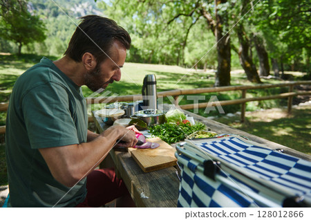 Man Preparing Fresh Vegetables Outdoors in a Scenic Park Setting Man Preparing Fresh Vegetables Outdoors in a Scenic Park Setting 128012866