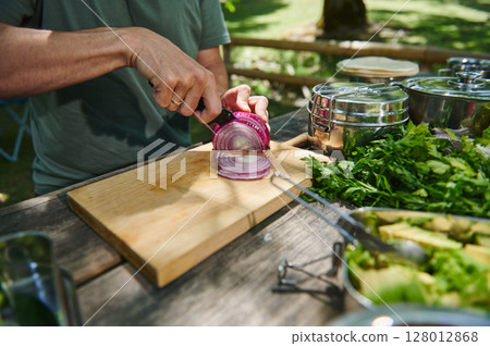 Person Cutting Fresh Red Onion on a Wooden Cutting Board Outdoors During a Picnic Person Cutting Fresh Red Onion on a Wooden Cutting Board Outdoors During a Picnic 128012868