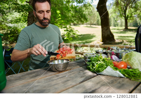 Man Preparing Fresh Vegetable Salad Outdoors in a Park with Scenic Background Man Preparing Fresh Vegetable Salad Outdoors in a Park with Scenic Background 128012881