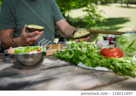 Preparing a Fresh Salad With Avocado Outdoors on a Sunny Day Preparing a Fresh Salad With Avocado Outdoors on a Sunny Day 128012897