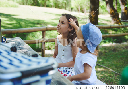 Children Enjoying an Outdoor Picnic in a Park Surrounded by Lush Greenery During a Sunny Day 128013103