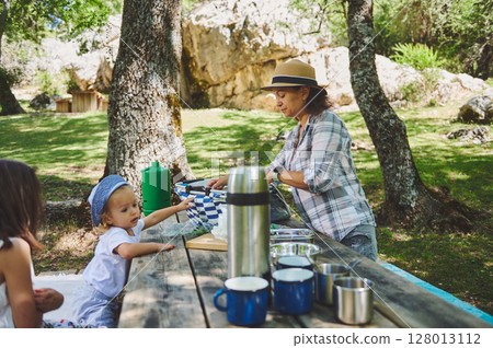Family Enjoying Outdoor Picnic in Forest Setting with Bright Daylight Family Enjoying Outdoor Picnic in Forest Setting with Bright Daylight 128013112