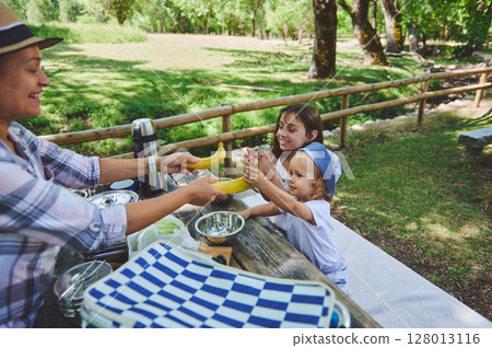 Family Picnic Outdoors in a Scenic Park with Cheerful Interaction 128013116