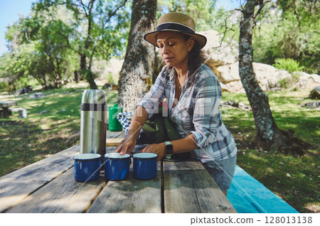 Woman Preparing Hot Drinks Outdoors at a Wooden Picnic Table in Nature 128013138
