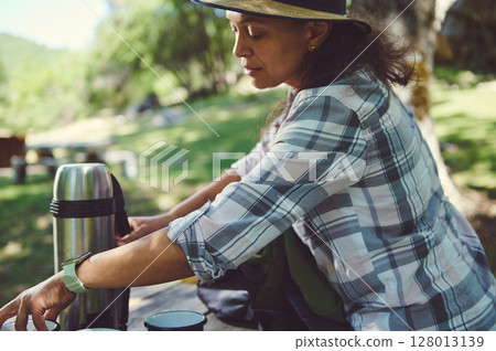 Woman in Outdoor Setting Preparing a Warm Beverage on a Sunny Day 128013139