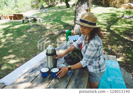 Woman Enjoying Outdoor Picnic Setting on Rustic Table in Nature Woman Enjoying Outdoor Picnic Setting on Rustic Table in Nature 128013140