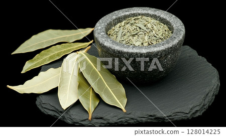 Dried bay leaves arranged on a dark slate surface, with a mortar and pestle nearby.  128014225
