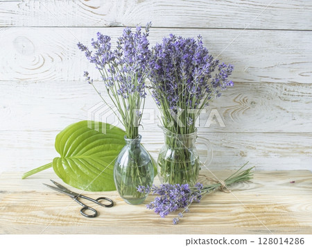 Bouquet of lavender flowers in a glass vase on a wooden background. Floral still life. 128014286