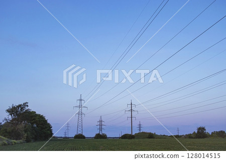 High voltage power transmission towers and power lines on green field at sunset. High voltage power transmission towers and power lines on green field at sunset. 128014515
