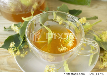 Linden tea in a glass cup with fresh linden flowers, on a wooden background. Medicinal herbal tea. Linden tea in a glass cup with fresh linden flowers, on a wooden background. Medicinal herbal tea. 128014792