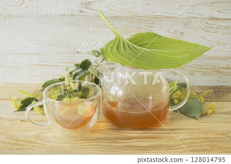 Linden tea in a glass cup with fresh linden flowers, on a wooden background. Medicinal herbal tea. 128014795
