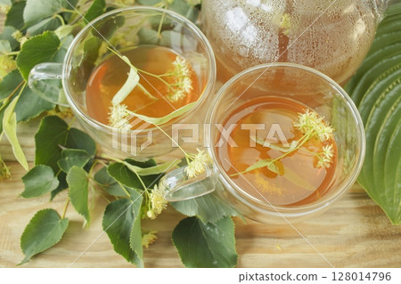 Linden tea in a glass cup with fresh linden flowers, on a wooden background. Medicinal herbal tea. Linden tea in a glass cup with fresh linden flowers, on a wooden background. Medicinal herbal tea. 128014796
