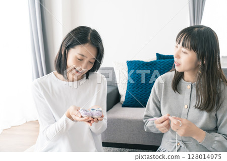 Mother and daughter knitting baby shoes 128014975