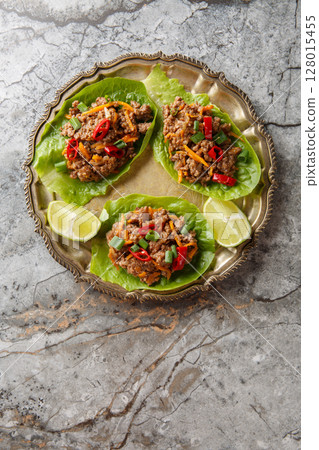 Asian Lettuce Wraps are filled with saucy, gingery beef and vegetables close-up on the plate. Vertical top view 128015455