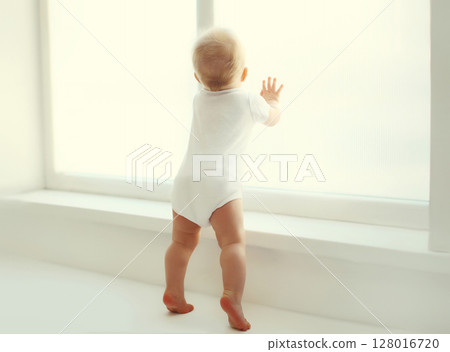 Little baby looking out the window in white room at home 128016720