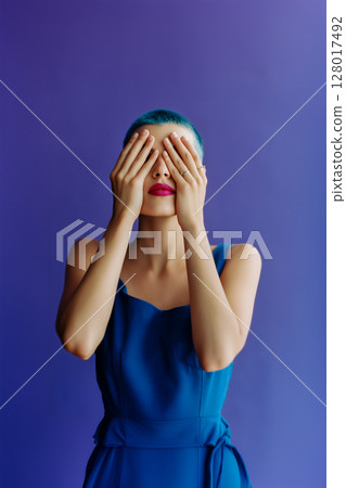 A woman in a blue dress is standing in front of a purple background A woman in a blue dress is standing in front of a purple background 128017492