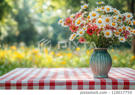 Picnic table with checkered tablecloth and a vase with flowers on a summer background. Retro-style. Mockup. Copy space. Picnic table with checkered tablecloth and a vase with flowers on a summer background. Retro-style. Mockup. Copy space. 128017759