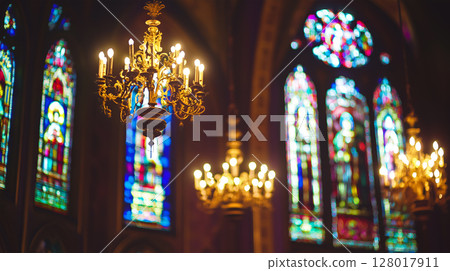 Elegant chandeliers illuminate stained glass windows in a historic church interior 128017911
