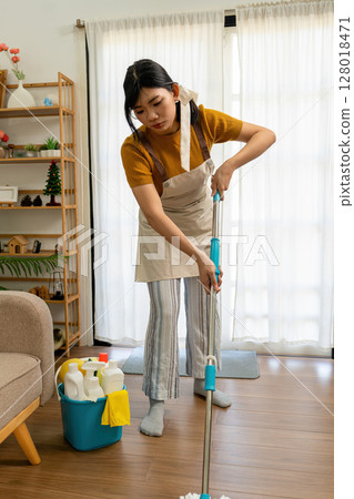 Young modern Asian woman doing house cleaning at home. Confident and independent homemaker maintaining a clean, stylish living space. 128018471