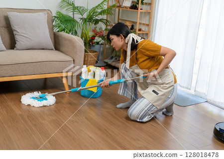 Young modern Asian woman doing house cleaning at home. Confident and independent homemaker maintaining a clean, stylish living space. Young modern Asian woman doing house cleaning at home. Confident and independent homemaker maintaining a clean, stylish living space. 128018478