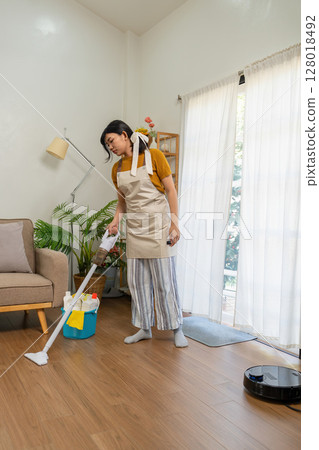 Young modern Asian woman doing house cleaning at home. Confident and independent homemaker maintaining a clean, stylish living space. Young modern Asian woman doing house cleaning at home. Confident and independent homemaker maintaining a clean, stylish living space. 128018492