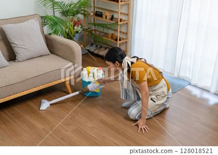 Young modern Asian woman doing house cleaning at home. Confident and independent homemaker maintaining a clean, stylish living space. Young modern Asian woman doing house cleaning at home. Confident and independent homemaker maintaining a clean, stylish living space. 128018521
