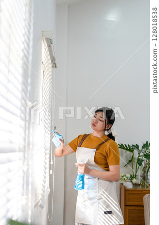 Young modern Asian woman doing house cleaning at home. Confident and independent homemaker maintaining a clean, stylish living space. Young modern Asian woman doing house cleaning at home. Confident and independent homemaker maintaining a clean, stylish living space. 128018538
