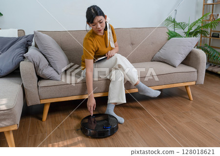 Young modern Asian woman doing house cleaning at home. Confident and independent homemaker maintaining a clean, stylish living space. Young modern Asian woman doing house cleaning at home. Confident and independent homemaker maintaining a clean, stylish living space. 128018621