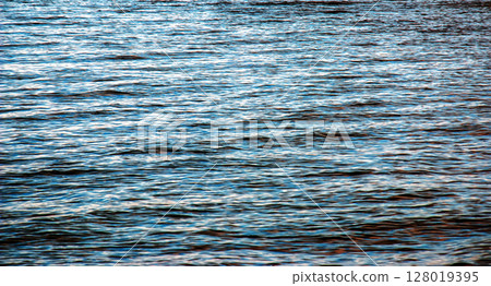 Water background of lake Traunsee in the Alps. The colorful texture of reflections of a clear mountain lake. Texture of water with reflections. Water background of lake Traunsee in the Alps. The colorful texture of reflections of a clear mountain lake. Texture of water with reflections. 128019395